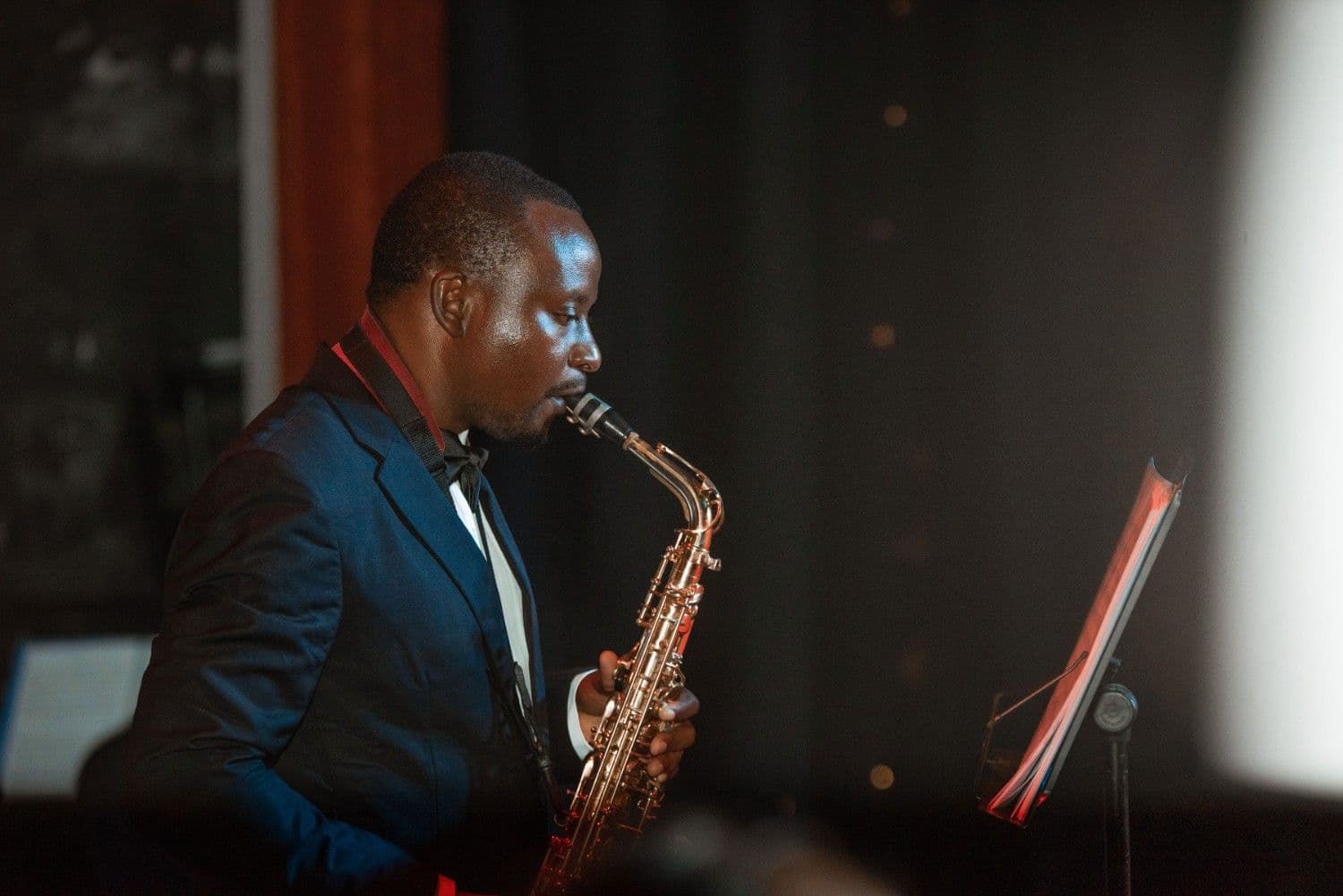 A musician in a tuxedo playing saxophone on a dark concert stage
