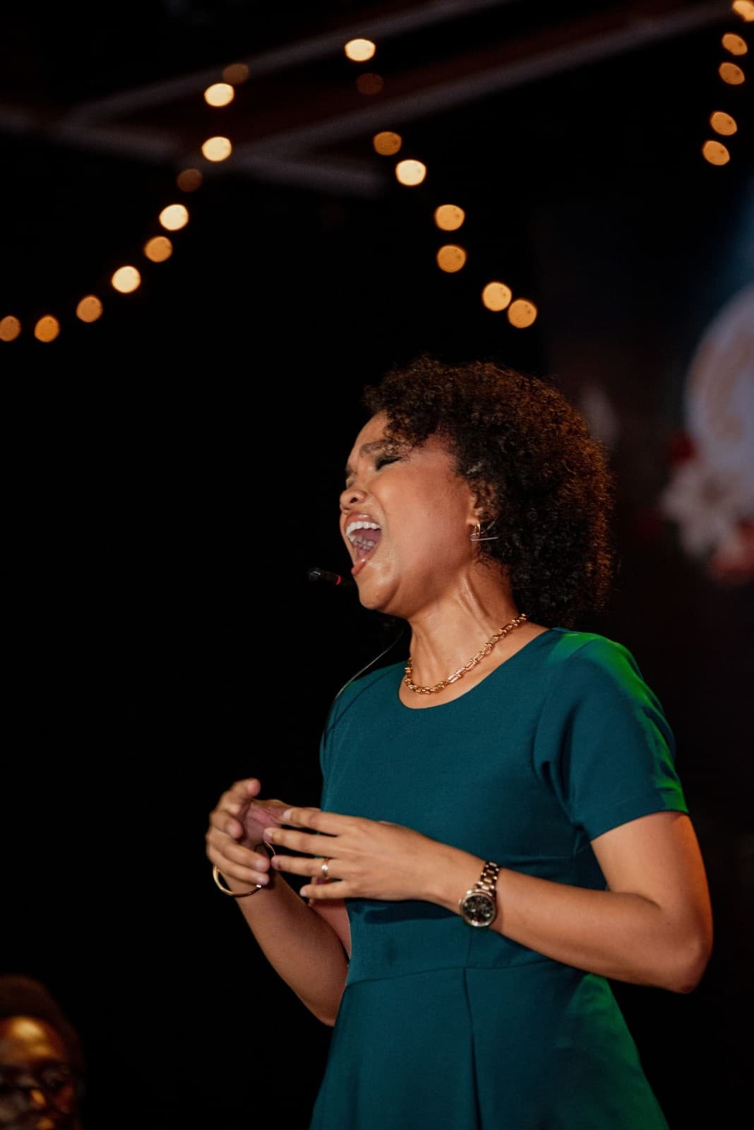 A soloist in an emerald dress singing against festive stage lights