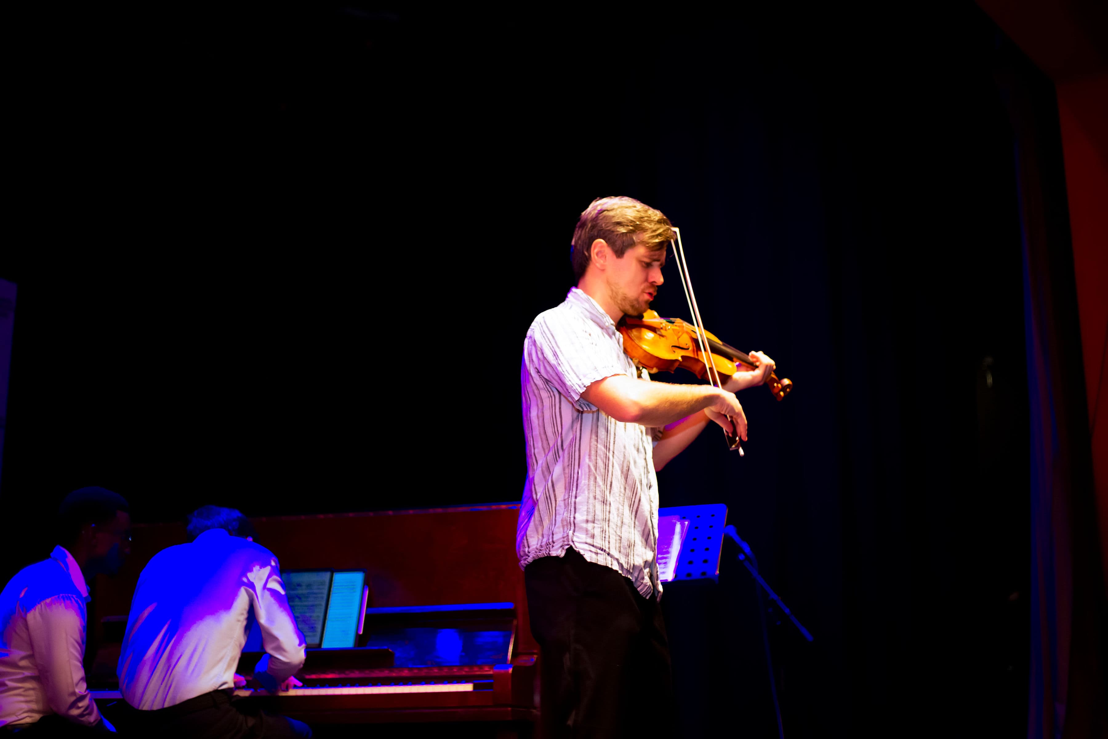 Violinist performing under warm stage light with piano accompaniment
